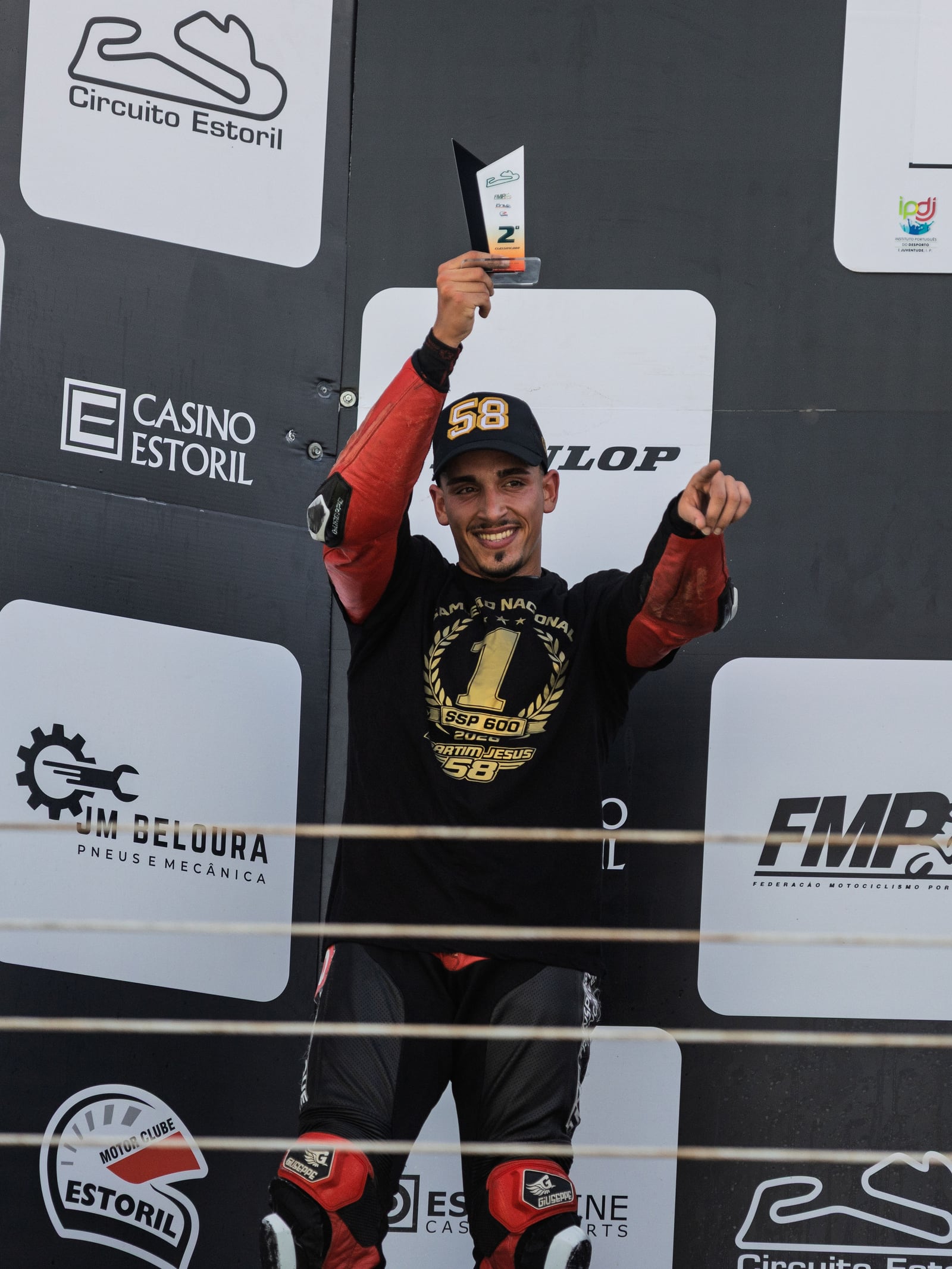 O Martim no pódio do Estoril, de troféu no ar e camisola de campeão, a apontar para a câmara
