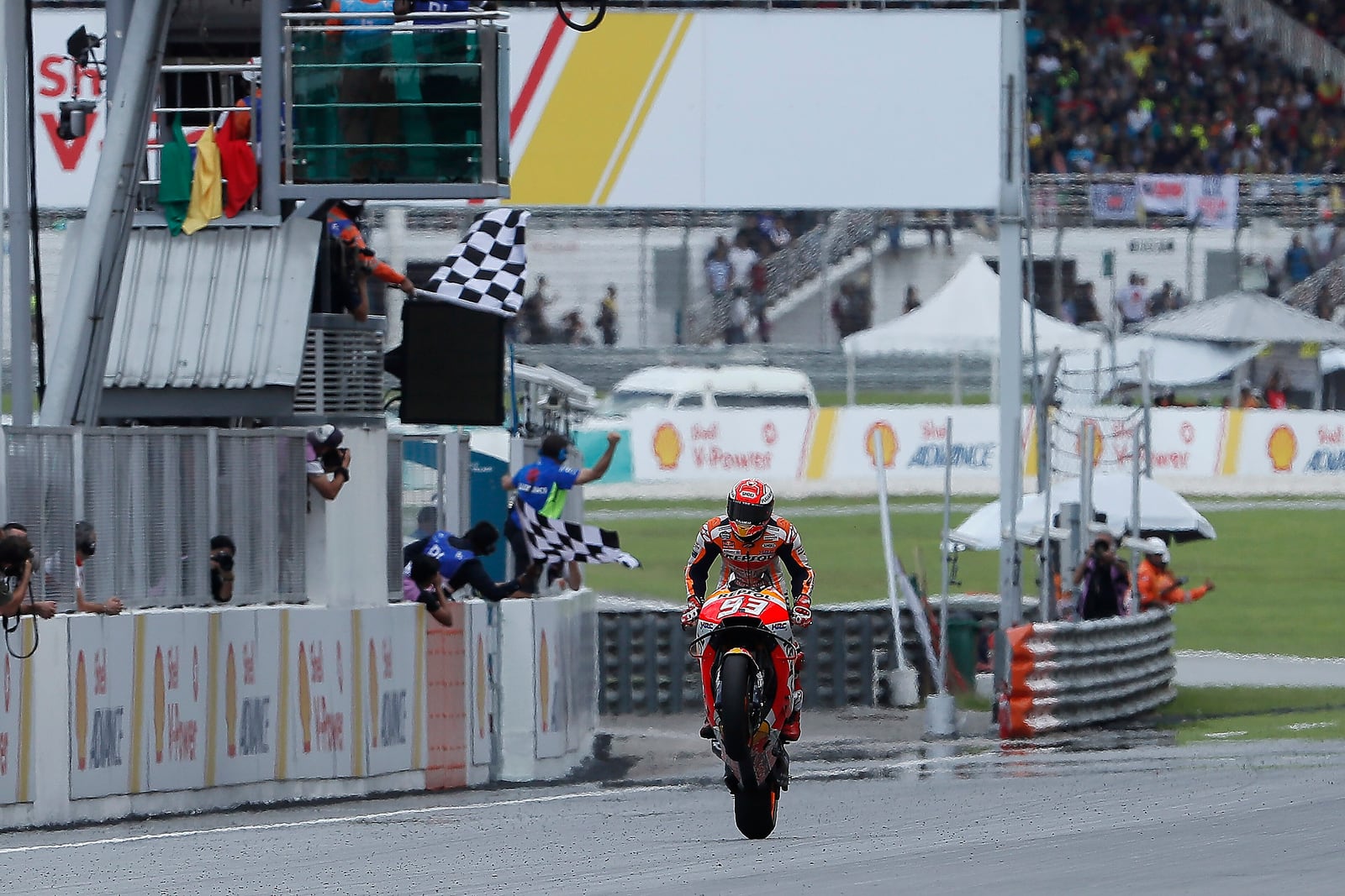 Marc Márquez a cruzar a meta em Sepang com a roda da frente no ar, ao lado da bandeira de xadrez